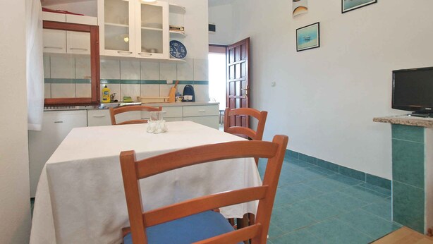 A dining area with a table and chairs, a kitchen in the background, and a television on a stand. - Studio with sea view and air conditioning (Peroj)