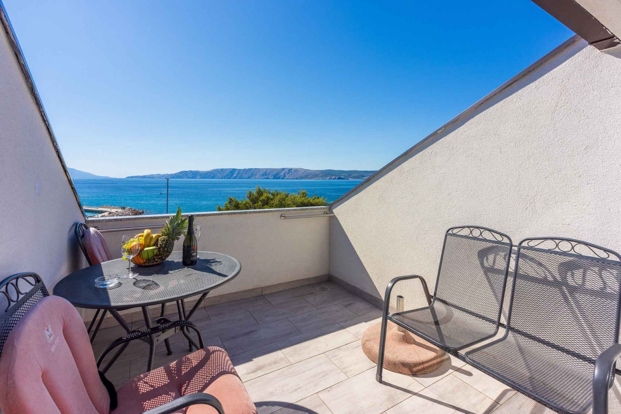 Un balcon avec une table, des chaises et une vue sur la mer.