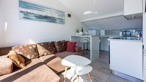 Un salon moderne avec un canapé, une petite table blanche et un coin cuisine équipé d’un réfrigérateur et d’un four à micro-ondes.