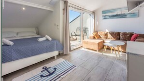 Une chambre à coucher comprenant un lit, un canapé, une petite table et une porte-fenêtre coulissante donnant sur un balcon.