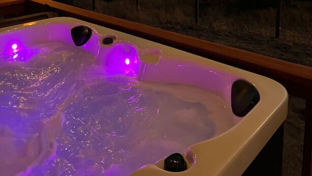 A hot tub with purple lighting, set against a sunset view.