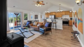A spacious living area with a fireplace, a sofa, and a coffee table. There is a kitchen with wooden cabinets and a refrigerator.