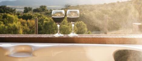 Un jacuzzi con dos copas de vino, rodeado de una vista panorámica de montañas y vegetación.