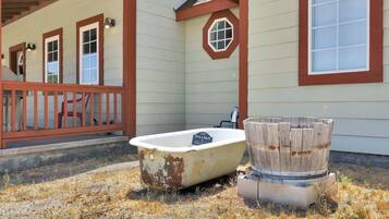 Un décor extérieur rustique agrémenté d’une baignoire ancienne et d’un tonneau en bois, évoquant un lieu chargé d’histoire ou un établissement à thème.