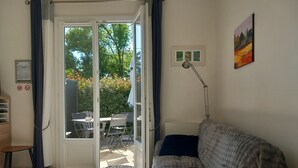Une pièce comprenant un canapé, un bureau, une chaise, une table à manger et une porte-fenêtre coulissante donnant sur un espace extérieur avec une table et des chaises.
