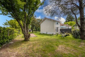 A house with a garden, a patio with chairs, and a pathway leading to the house.