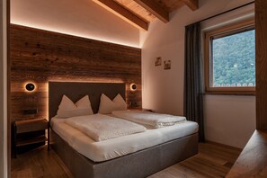 Een slaapkamer met een houten hoofdbord, een bed met witte lakens, een nachtkastje en een raam met uitzicht op een bos.