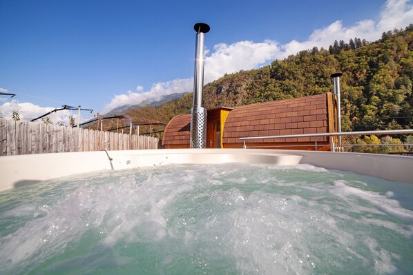 A hot tub with a wooden fence and a mountain backdrop. - Chalet Jasmin – Spacious Chalet with Garden and Olive Tree, Ideal for Relaxing Getaways (Rifiano)