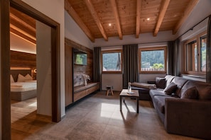 A modern living room with a wooden ceiling, a sofa, a coffee table, and a view of a forested area through large windows.
