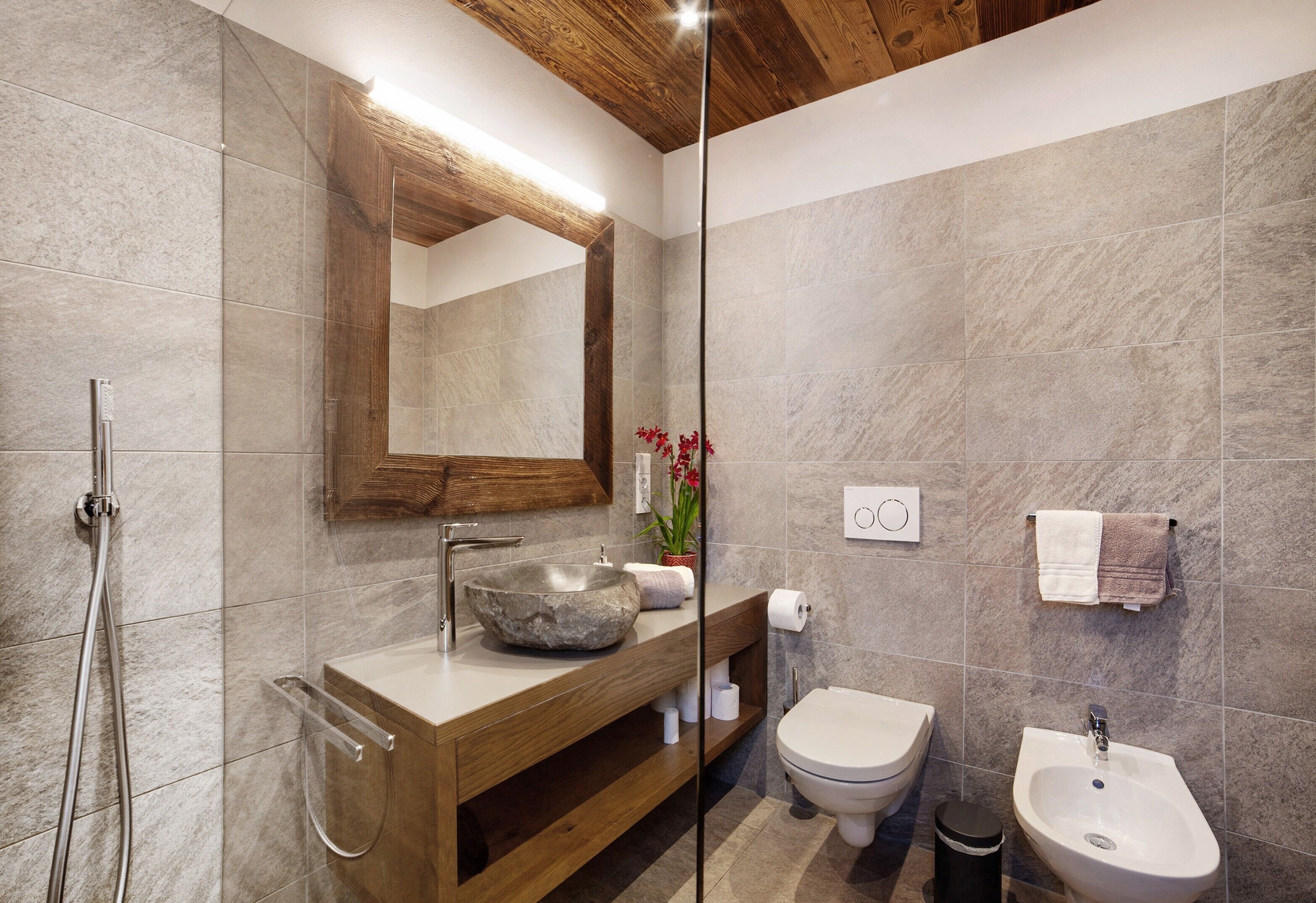 Un bagno moderno con un mobile bagno in legno, uno specchio grande, un lavabo in pietra, un water e un bidet.