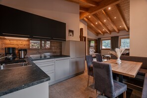 A modern kitchen with a built-in oven, a coffee maker, and a sink. There is a dining area with a table and chairs. - Chalet Rose with Two Split-Level Terraces and Maximum Privacy (Rifiano)