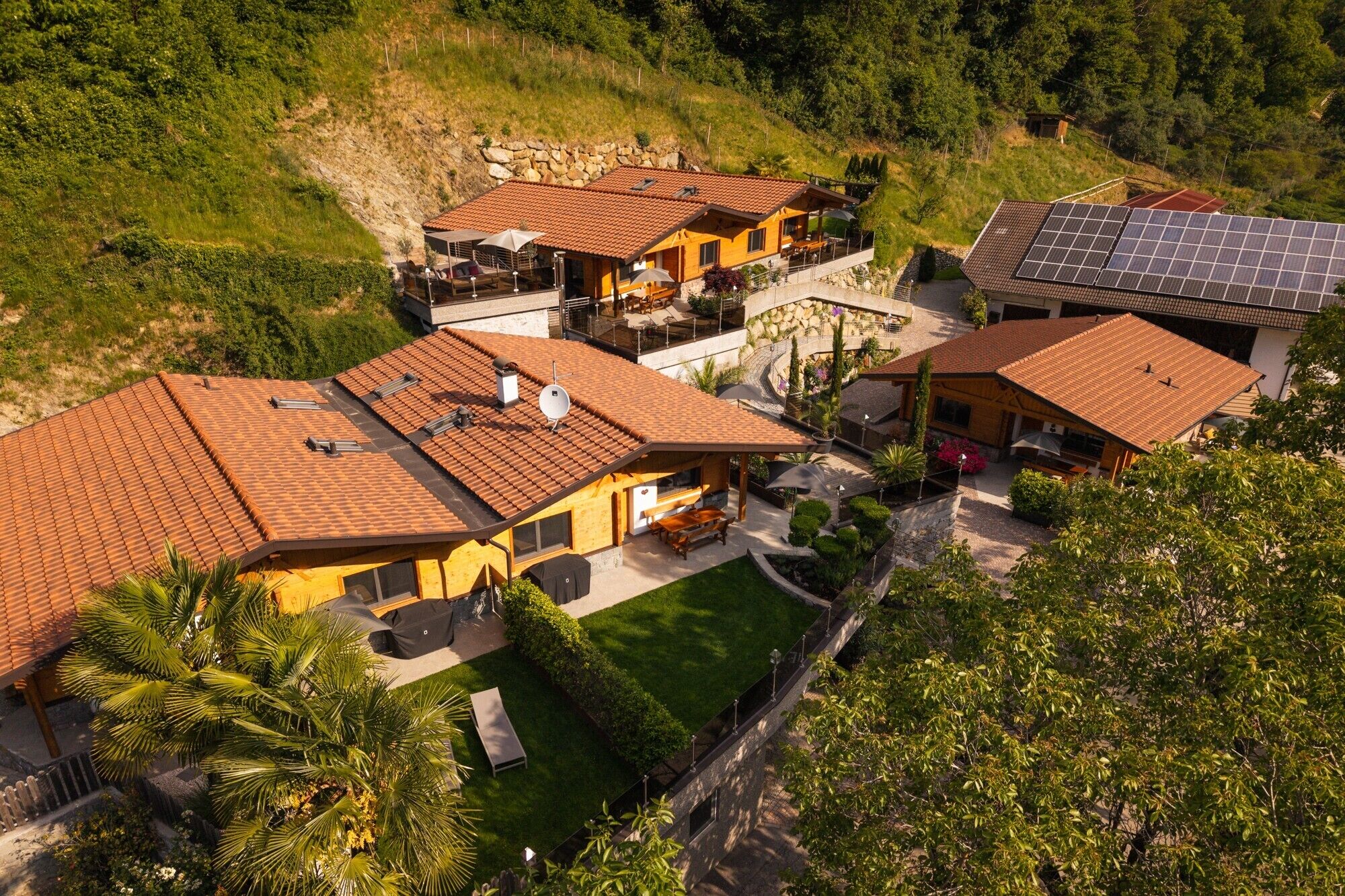 Il s’agit d’une propriété résidentielle comprenant plusieurs maisons, chacune dotée d’un toit en tuiles, d’espaces extérieurs aménagés et de panneaux solaires.