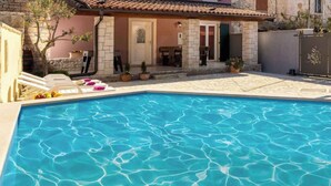 A swimming pool with a stone wall on one side and a building with a tiled roof in the background. - Villa with terrace for 2 people (Orbanići)