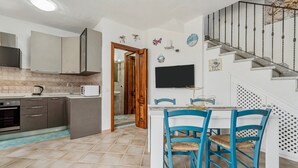 Een keuken met kasten, een magnetron en een fornuis. Er is een eethoek met een tafel en stoelen. Een televisie is aan de muur bevestigd.