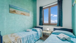 Een kamer met twee bedden, een raam met gordijnen, een tafeltje met een lamp en een schilderij aan de muur.