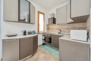 Una cucina compatta con forno a microonde, bollitore e macchina del caffè sul piano di lavoro, forno integrato e finestra vista.