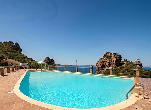 A swimming pool with a clear view of the sea and rocky hills in the background. - Villa la Perla e le Conchiglie Tanca Piras (NEBIDA)