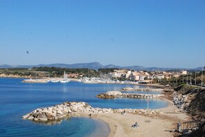 A coastal town with a clear blue sea, rocky beach, and buildings in the background.