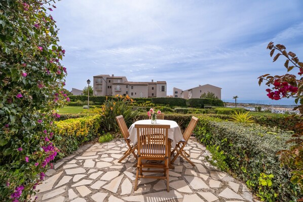 A patio with a round table and chairs, a stone pathway, and a view of buildings in the background.