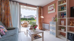 A living room with a sofa, a coffee table, a TV stand, and a view of the outside. - Magnificent T2 Apartment with Sea View and Wi-Fi (Six-Fours-les-Plages)