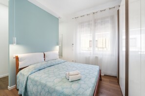 Une chambre à coucher comprenant un lit, une table de chevet, une commode, une fenêtre avec des rideaux et un luminaire suspendu.