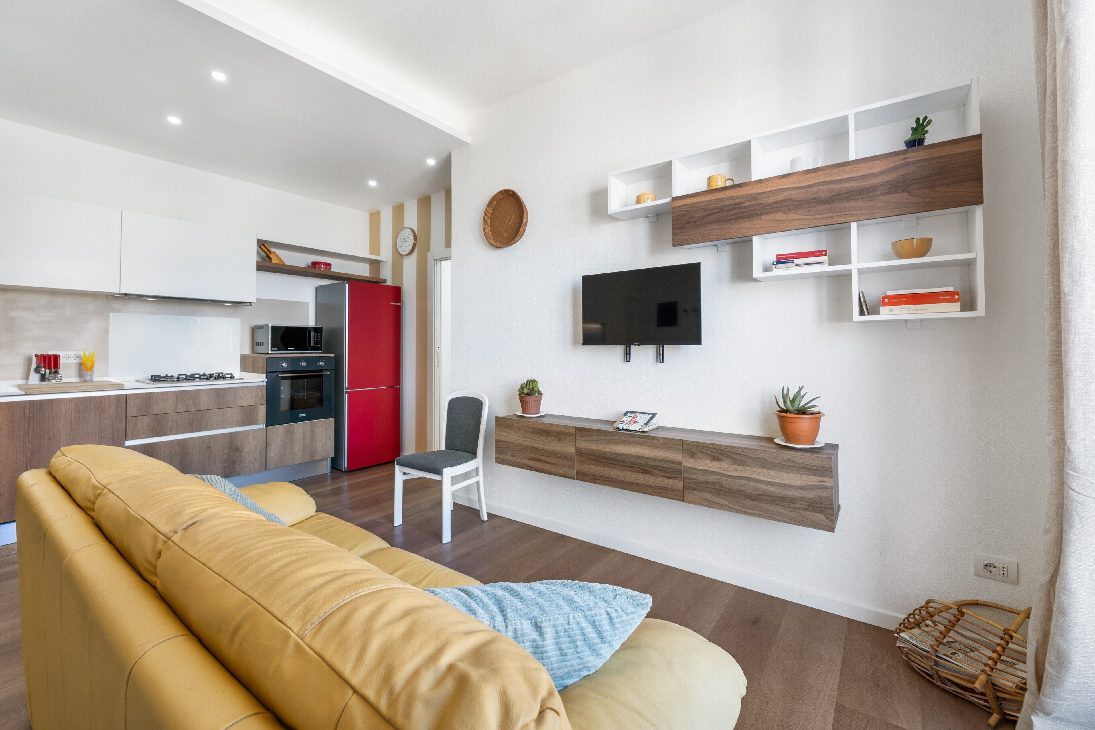 Una sala de estar moderna con un sofá, un televisor montado en la pared y una cocina al fondo.