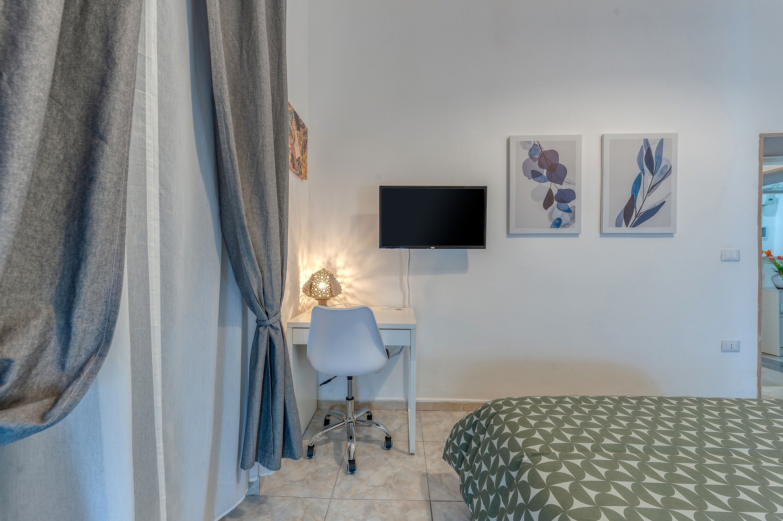 Een kamer met een bed, een bureau met stoel, een televisie en kunst aan de muur.