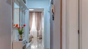 A hallway leading to a bedroom with a bed, a chair, a small table, and a vase with flowers. - Apartment 'Nest 27' with Private Terrace, Wi-Fi and Air Conditioning (Lecce)