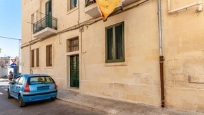 A blue car parked on a street, a building with a balcony, and a yellow flag. - Apartment 'Nest 27' with Private Terrace, Wi-Fi and Air Conditioning (Lecce)