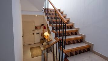A staircase with wooden steps and black railings leading to a landing with a door, a wall-mounted light, and a small table with a lamp.