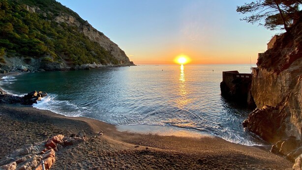 Ein Küsten-Sonnenuntergang mit felsigen Klippen und ruhiger See.