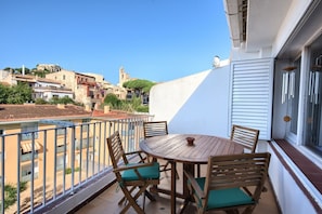 Un balcon avec une table ronde en bois et quatre chaises, d’où l’on peut admirer une vue sur la ville, avec ses bâtiments et le clocher d’une église.