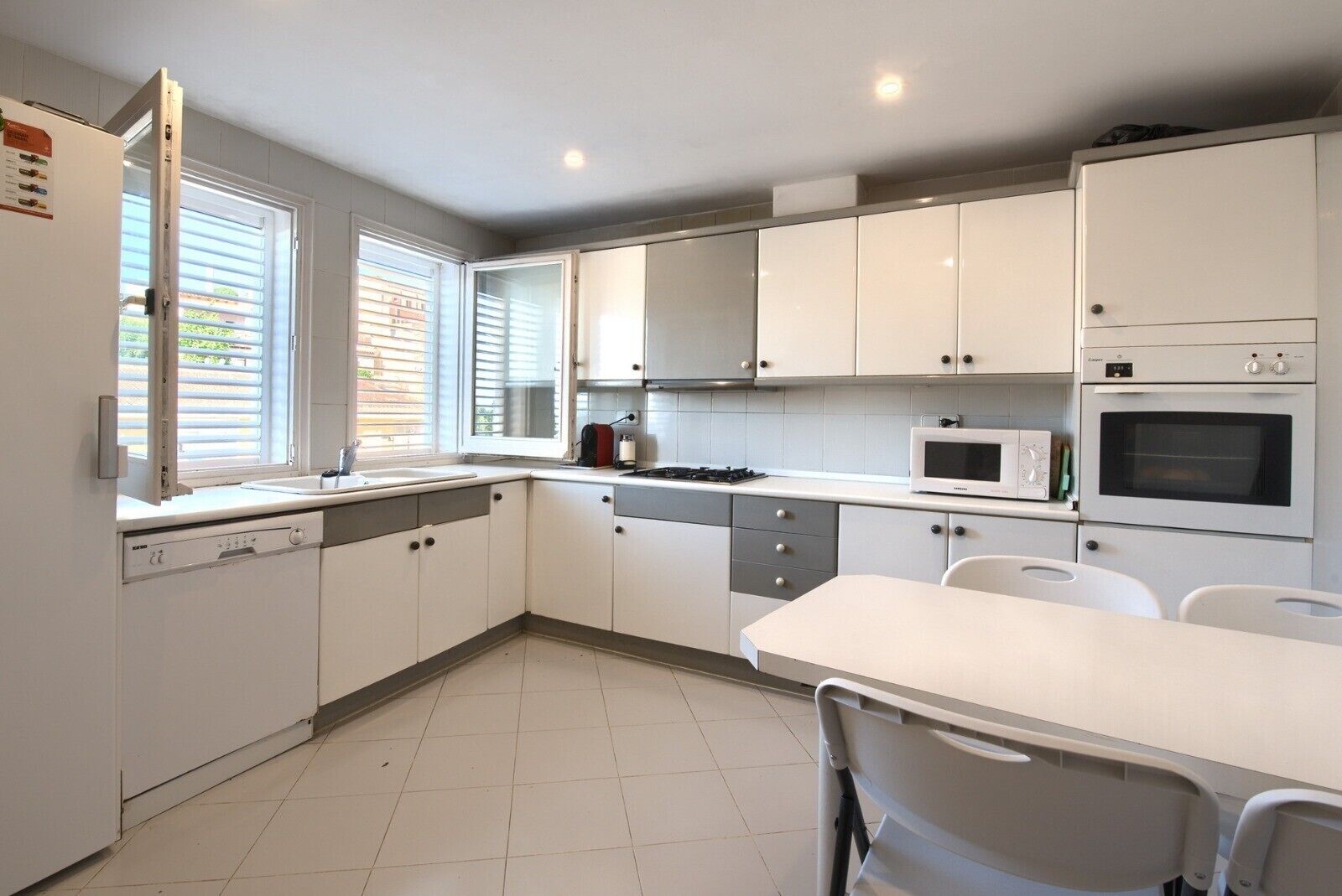 A modern kitchen with white cabinets, a dishwasher, a microwave, an oven, and a dining area with a table and chairs.