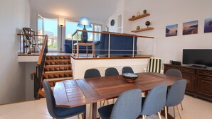 Ein zeitgemäßer Wohnraum mit Essbereich, Treppe und Fernseher.