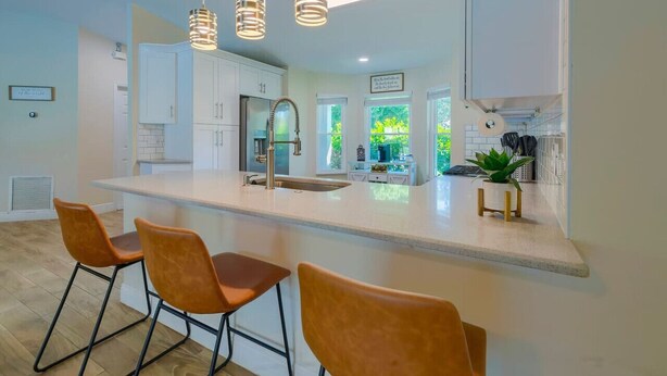 A modern kitchen with a central island, bar stools, pendant lighting, and a view of greenery outside. - New! Resort Style Oasis ~ Heated Pool & Game Room (Minneola)