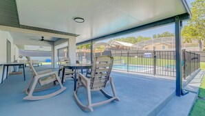 An outdoor patio area with a table and chairs, a ceiling fan, and a view of a fenced pool area. - New! Resort Style Oasis ~ Heated Pool & Game Room (Minneola)