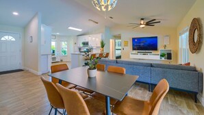 A modern kitchen with white cabinets, a dining area with a table and chairs, and a living area with a sofa and television. - New! Resort Style Oasis ~ Heated Pool & Game Room (Minneola)