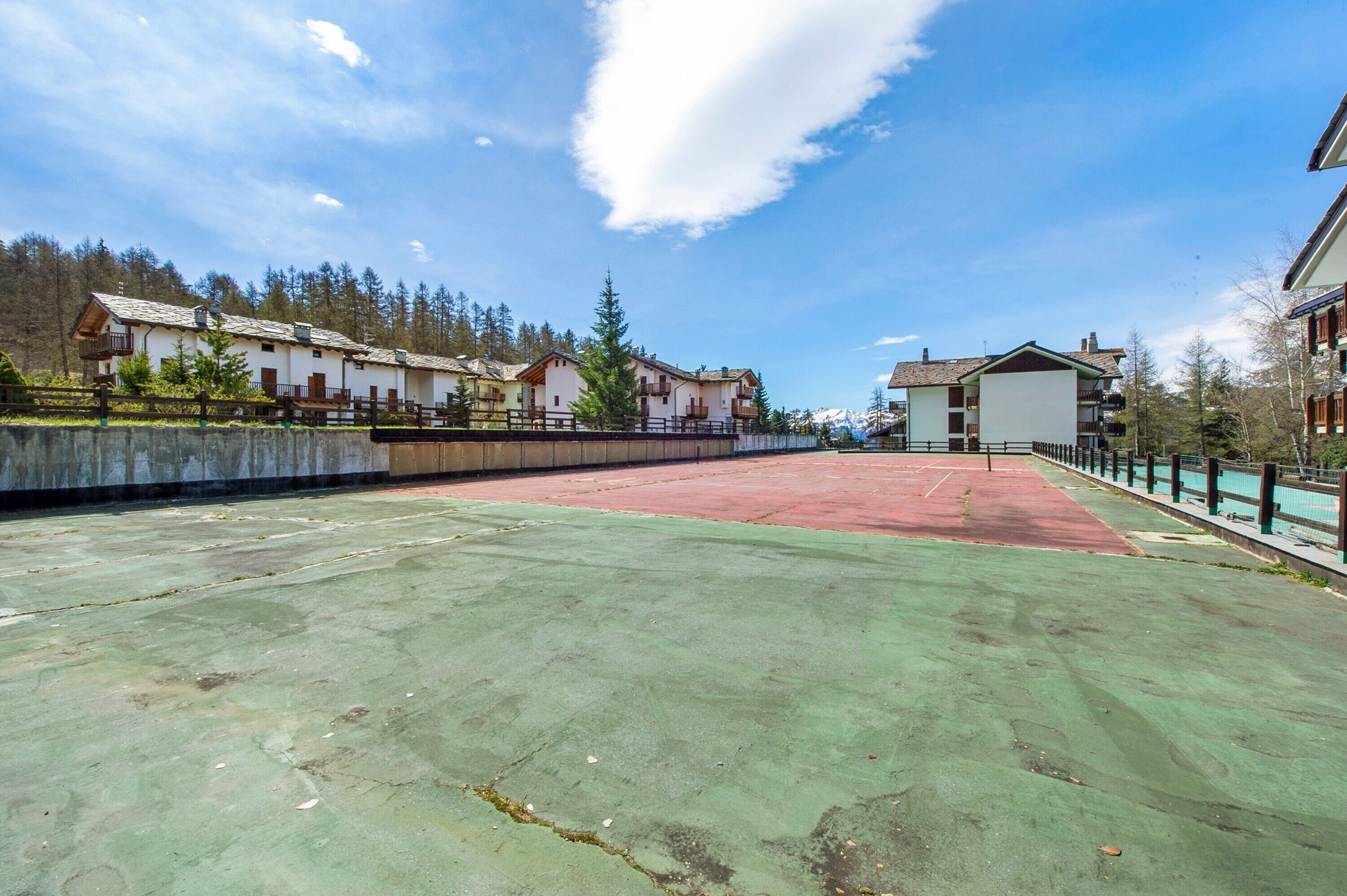 Ein Tennisplatz mit grüner Belag, umgeben von Gebäuden mit Balkonen und einer Bergkulisse.