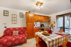 Eine kleine Küche mit Holzausstattung, einem Esstisch mit kariertem Tischläufer und einem roten Sofa mit gemusterten Kissen.