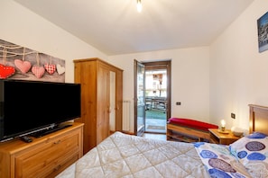 Ein Schlafzimmer mit Fernseher, Holzschrank und einem Bett mit gemusterten Betttextilien.