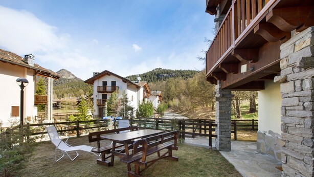 Une terrasse avec une table et des bancs en bois, entourée de murs en pierre et d’une clôture en bois.