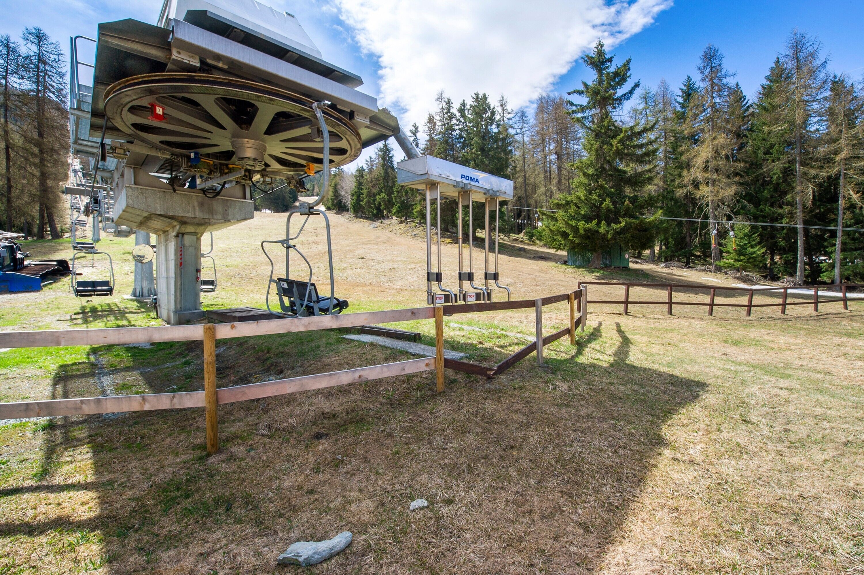 Eine Seilbahn mit Sesseln, einer Holzzahlung und einem Pavillon mit der Aufschrift 'POMA' in einem bewaldeten Gebiet.
