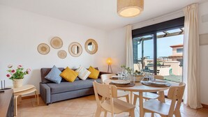 Una sala de estar con sofá, mesa de comedor, sillas y un amplio ventanal con cortinas.