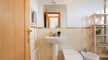 A bathroom with a wooden door, a pedestal sink, a bidet, and a mirror above the sink.