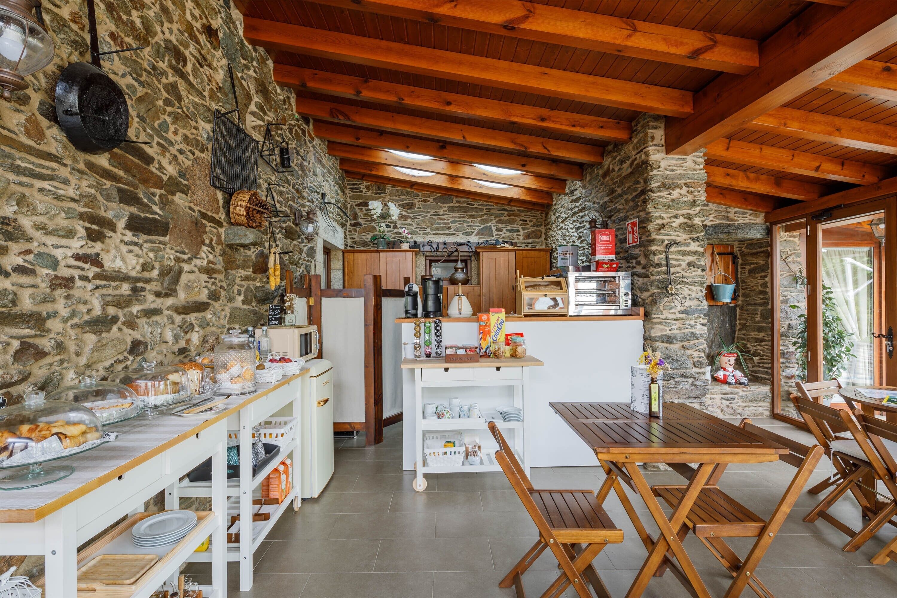 A rustic kitchen with stone walls, wooden beams, a central island, and a dining area with wooden tables and chairs.