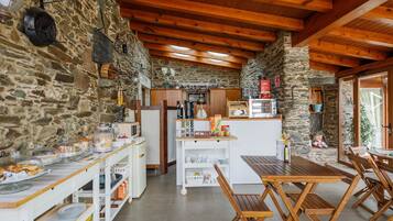 A rustic kitchen with stone walls, wooden beams, a central island, and a dining area with wooden tables and chairs.