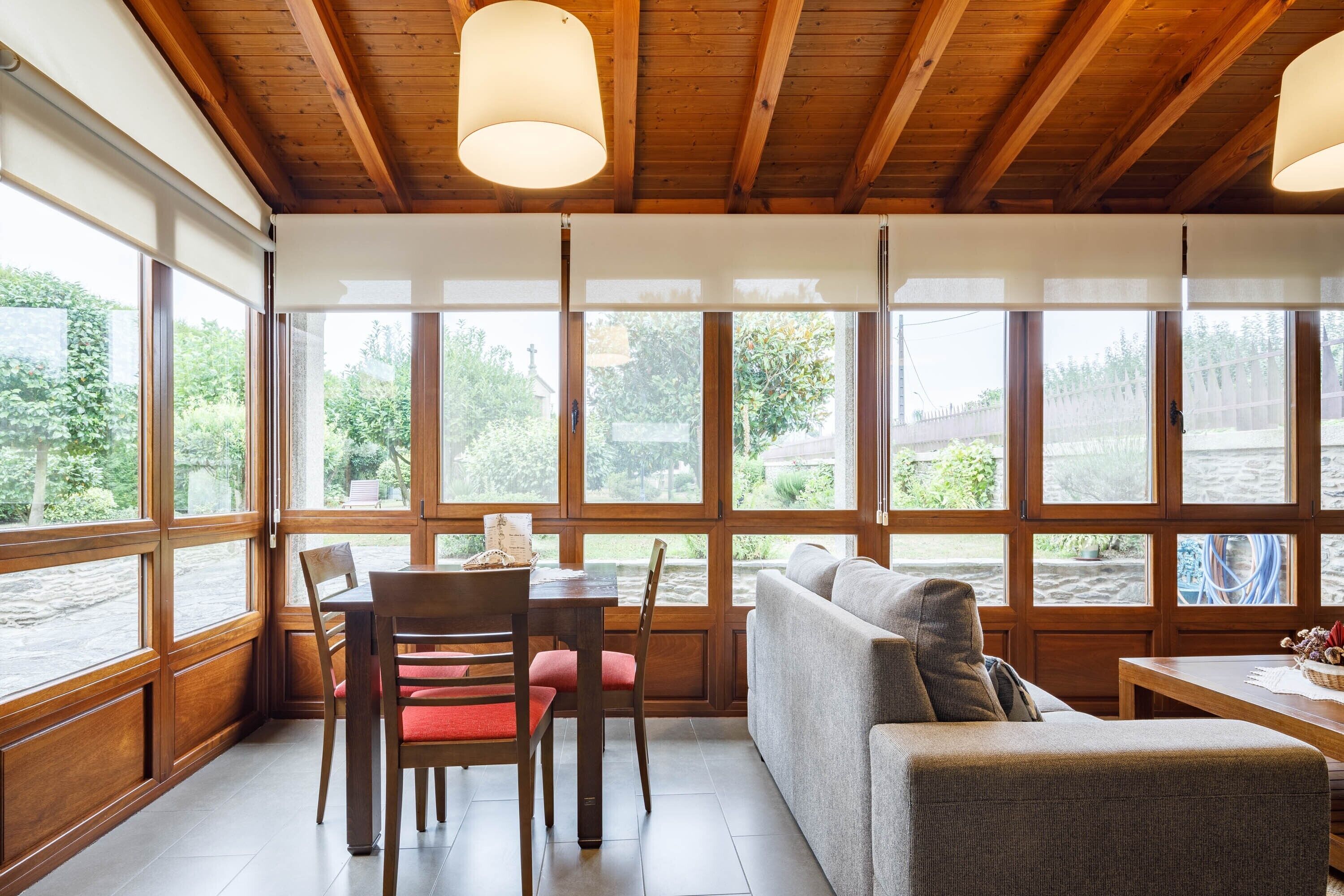 A room with a wooden ceiling, large windows, a sofa, a table, and chairs.