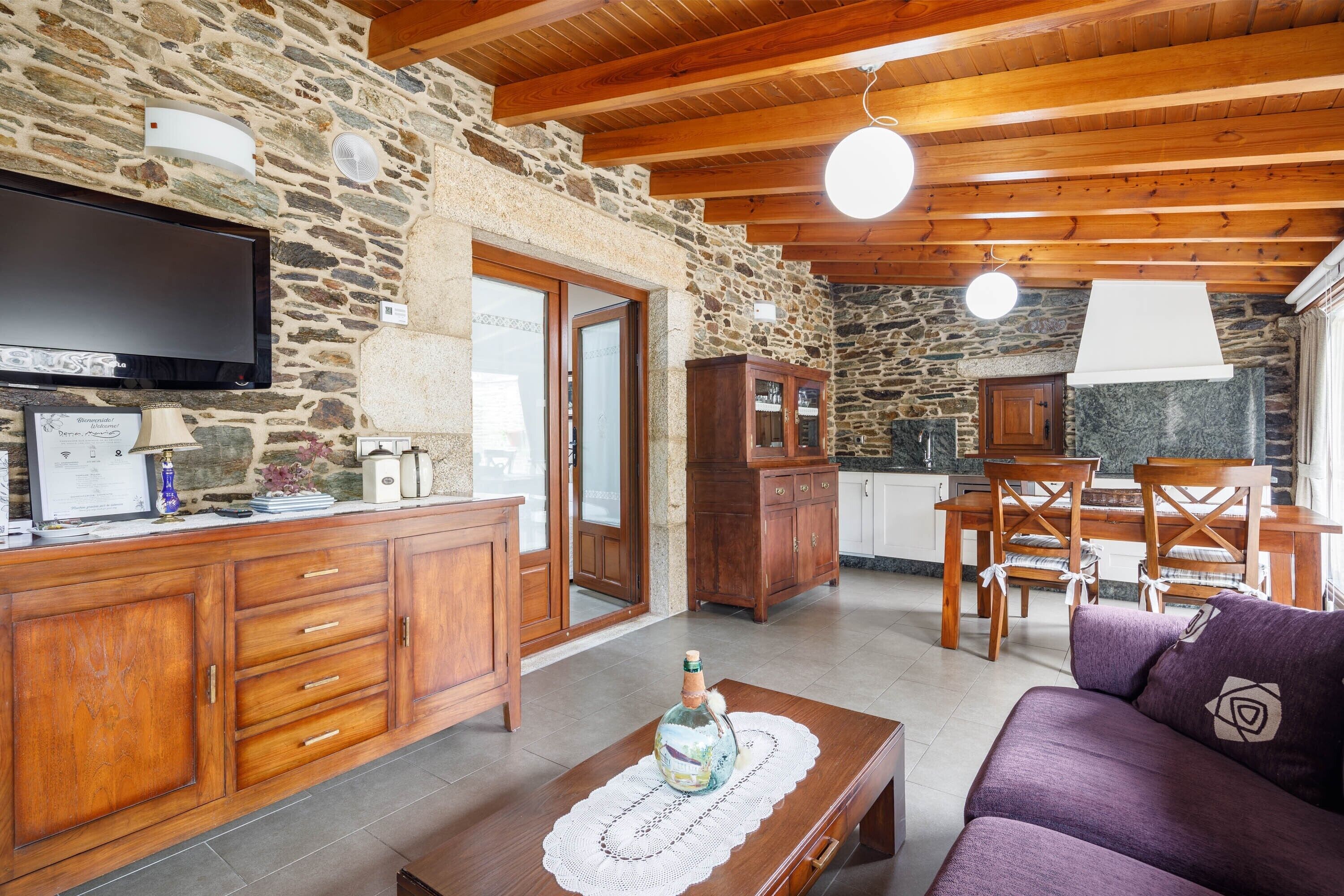 A cozy living area with a stone wall, wooden furniture, a flat-screen TV, and a dining table with chairs.