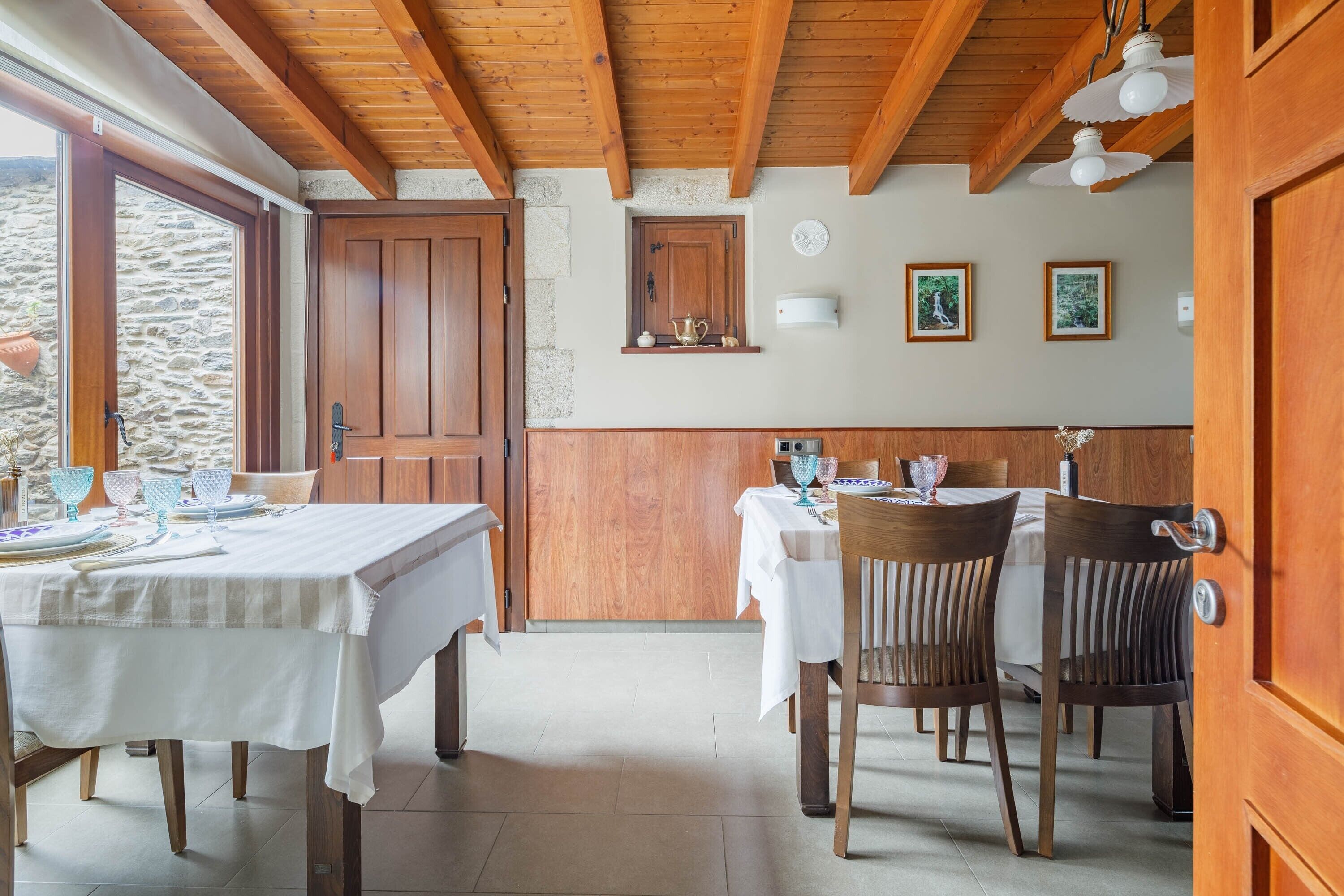 Un comedor con mesas y sillas de madera, una pared de piedra y vigas de madera en el techo.