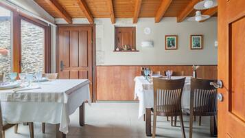 A dining area with wooden tables and chairs, a stone wall, and wooden ceiling beams.